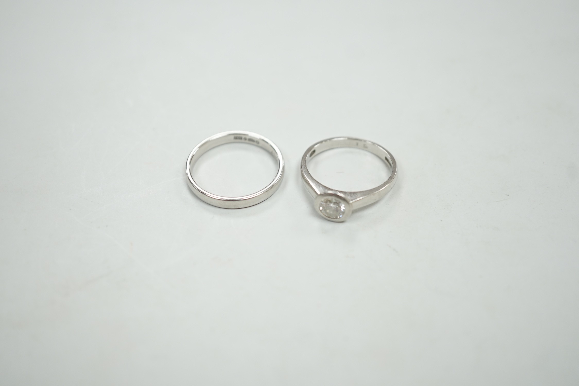 A modern platinum and collet set solitaire diamond ring, size M, gross weight 4.9 grams, together with a modern platinum wedding band, size N, 3.8 grams.